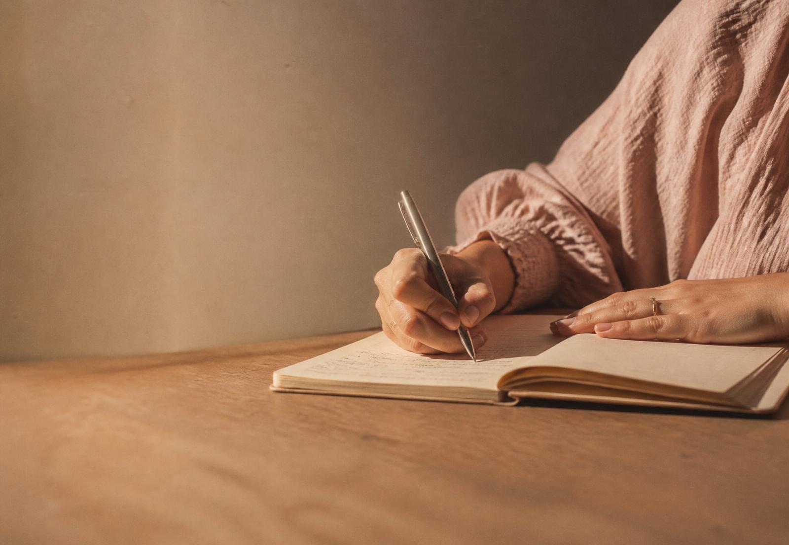 Mãos escrevendo à caneta em um caderno sobre mesa de madeira